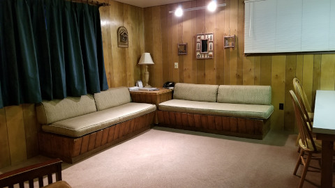 Two day couches along the wall in a larger living room. Off to the side between the living room and kitchen is a low bar to eat at. There are two big windows in the living room to let in lots of light.